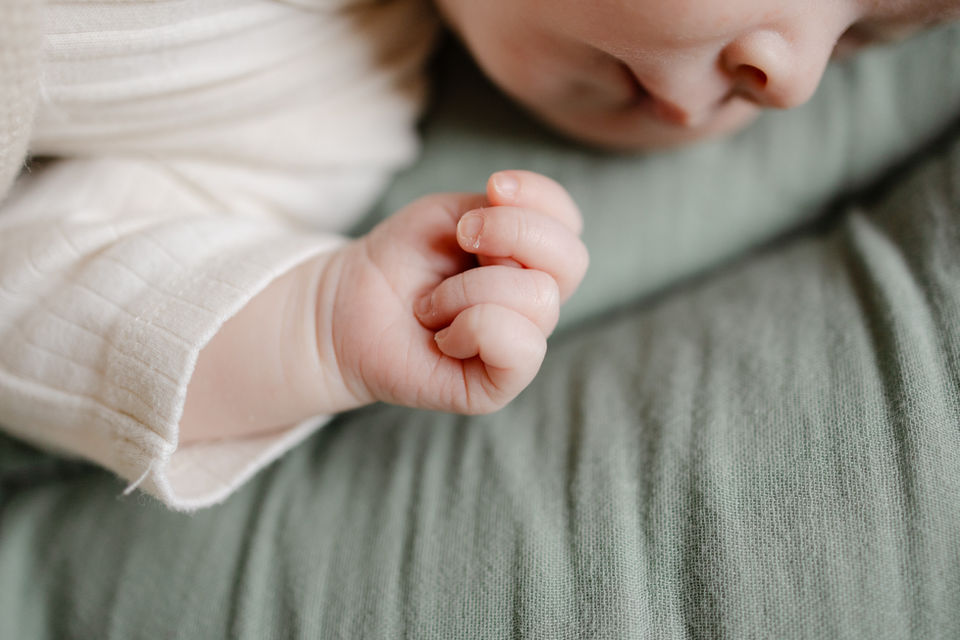 Newborn-Fotografin Mönchengladbach — Nahaufnahme winziger Babyfaust auf grünem Musselin, stimmungsvolles Neugeborenen-Shooting