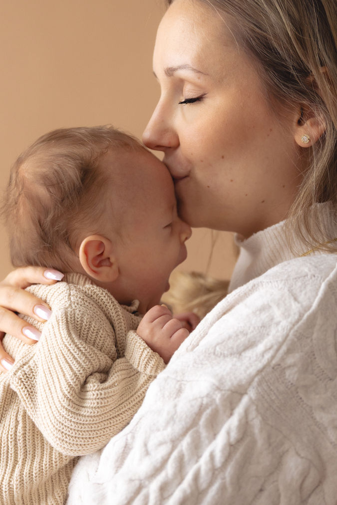 Newborn-Fotografie Mönchengladbach — Mutter gibt schlafendem Baby einen Kuss auf die Stirn, emotionales Neugeborenen-Shooting