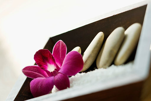 A pink flower rests next to spa stones in a wood box