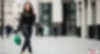 A stylish woman in a black lace top and leather pants walks confidently with a green handbag in a modern city setting.