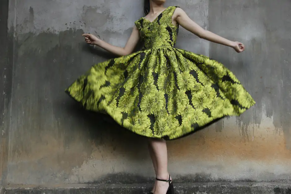 Woman twirling in a bold yellow and black floral dress with a full skirt, creating a striking, high-impact look that reflects a dramatic style.