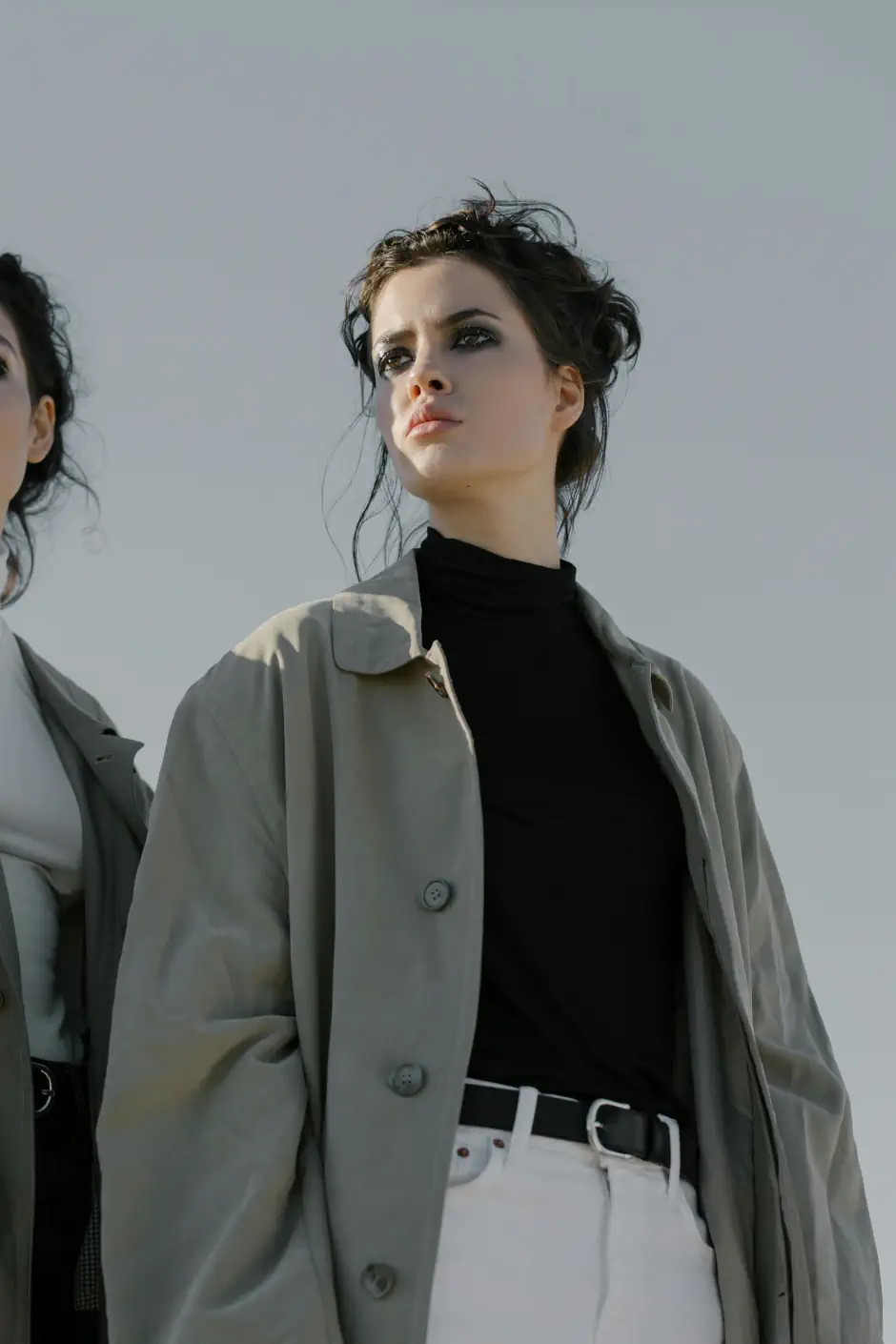 Woman in a light coat, black top and white trousers looking confidently into the distance, expressing a minimal, modern and effortless style.