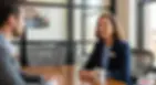 Female HR manager and male employee have a thoughtful conversation in a modern office, seated across a conference table.