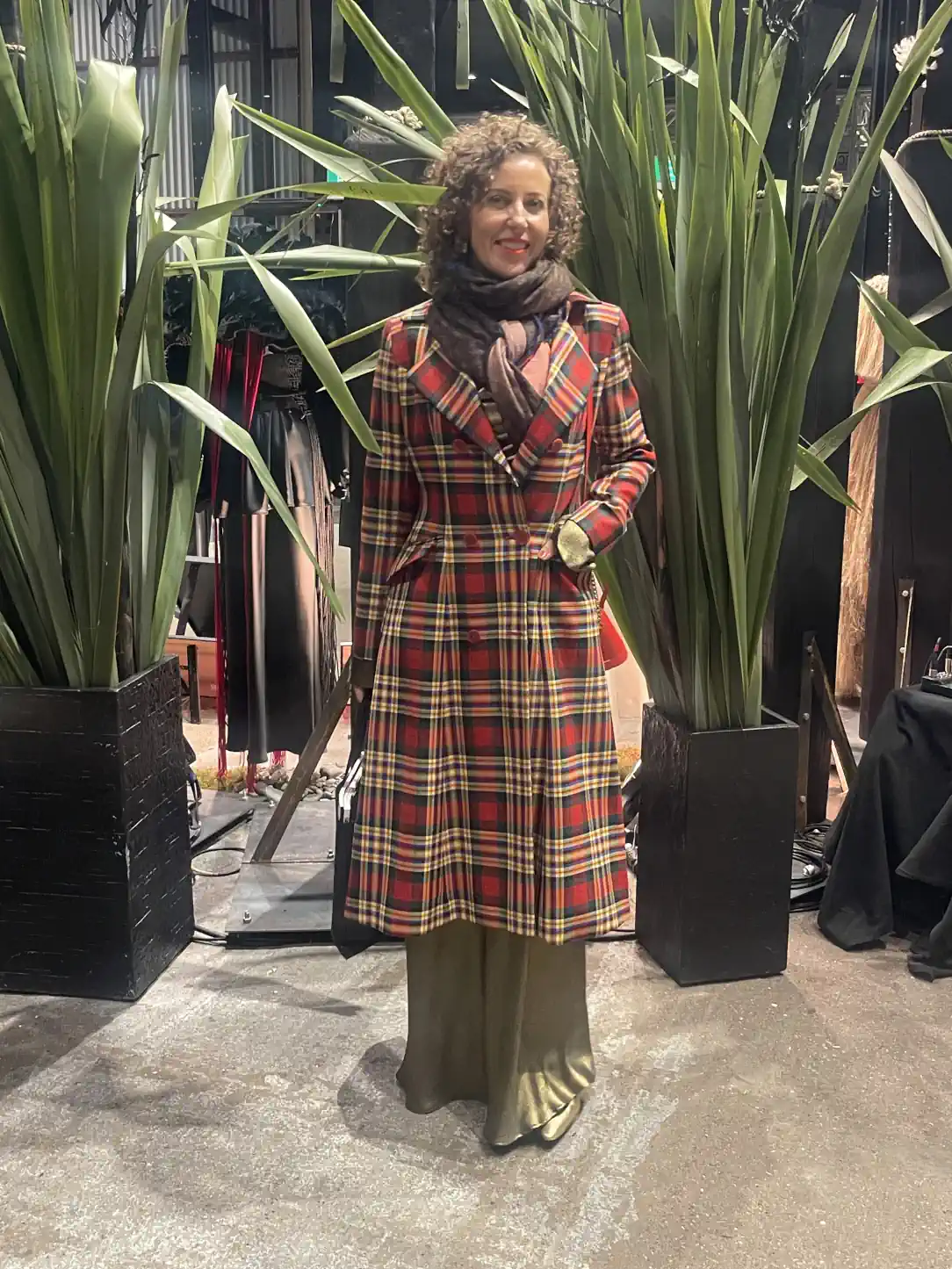 Stephanie Rumble in a tartan coat and scarf, layered over a satin dress, dressed warmly before the Karen Walker fashion show.