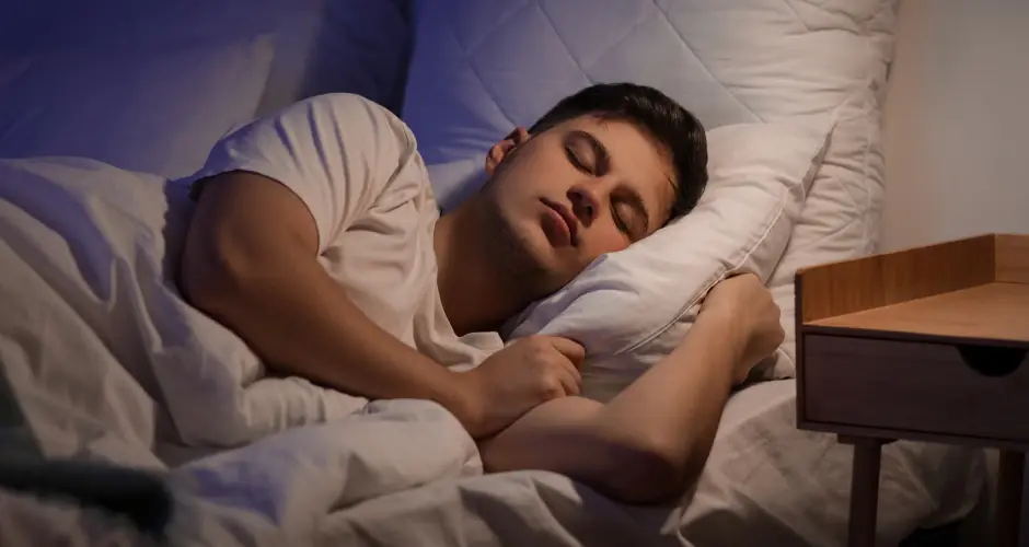 Man sleeping peacefully in bed at night, resting on a pillow in a calm bedroom with soft lighting.