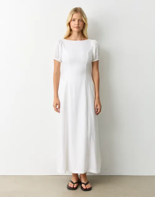Model wearing a cloud white long dress with puff sleeves, styled with flat sandals against a minimalist backdrop.