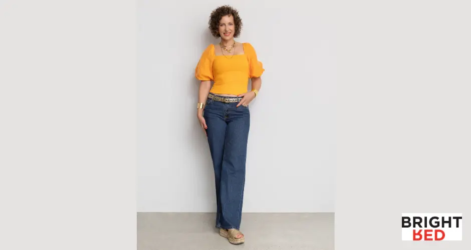 Stephanie Rumble wearing dark jeans and orange top, styled confidently in Bright Red brand image.