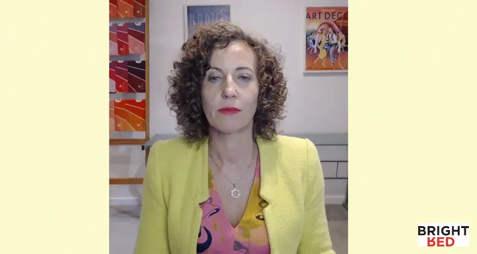Stephanie Rumble sitting calmly indoors, wearing a yellow blazer and patterned blouse, demonstrating mindful breathing.