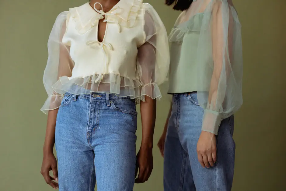 Two women wearing soft, sheer blouses with ruffled details paired with jeans, reflecting a delicate and romantic feminine style.