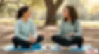 Two women sit cross-legged on yoga mats in a park, having a supportive conversation. They’re dressed in activewear with healthy snacks, a journal, and a phone nearby—symbolizing emotional support, habit building, and wellness coaching.