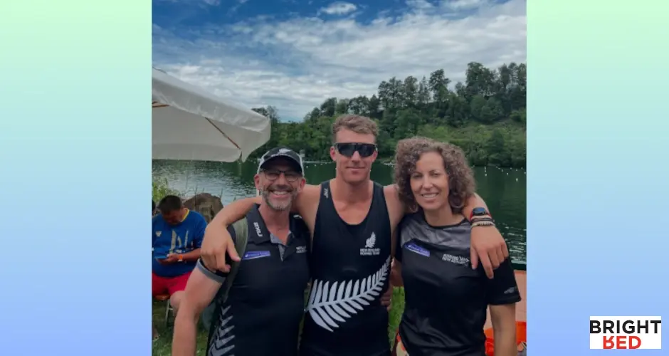 Zack stands outdoors with his parents by a lake, all smiling in New Zealand rowing gear, showing family support and pride.