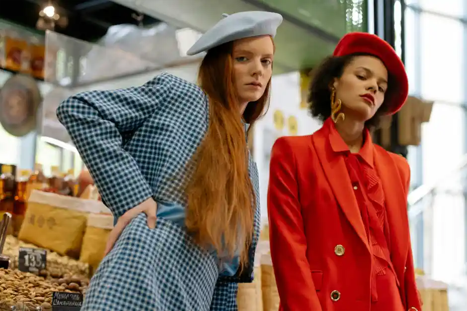 Two women in statement outfits and berets, one in blue checks and the other in vibrant red, showcasing bold, artistic and creative personal style.