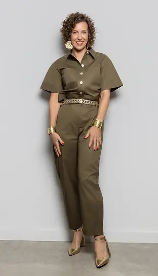 Stephanie Rumble wearing a tailored olive jumpsuit with gold accessories, standing confidently against a neutral background.