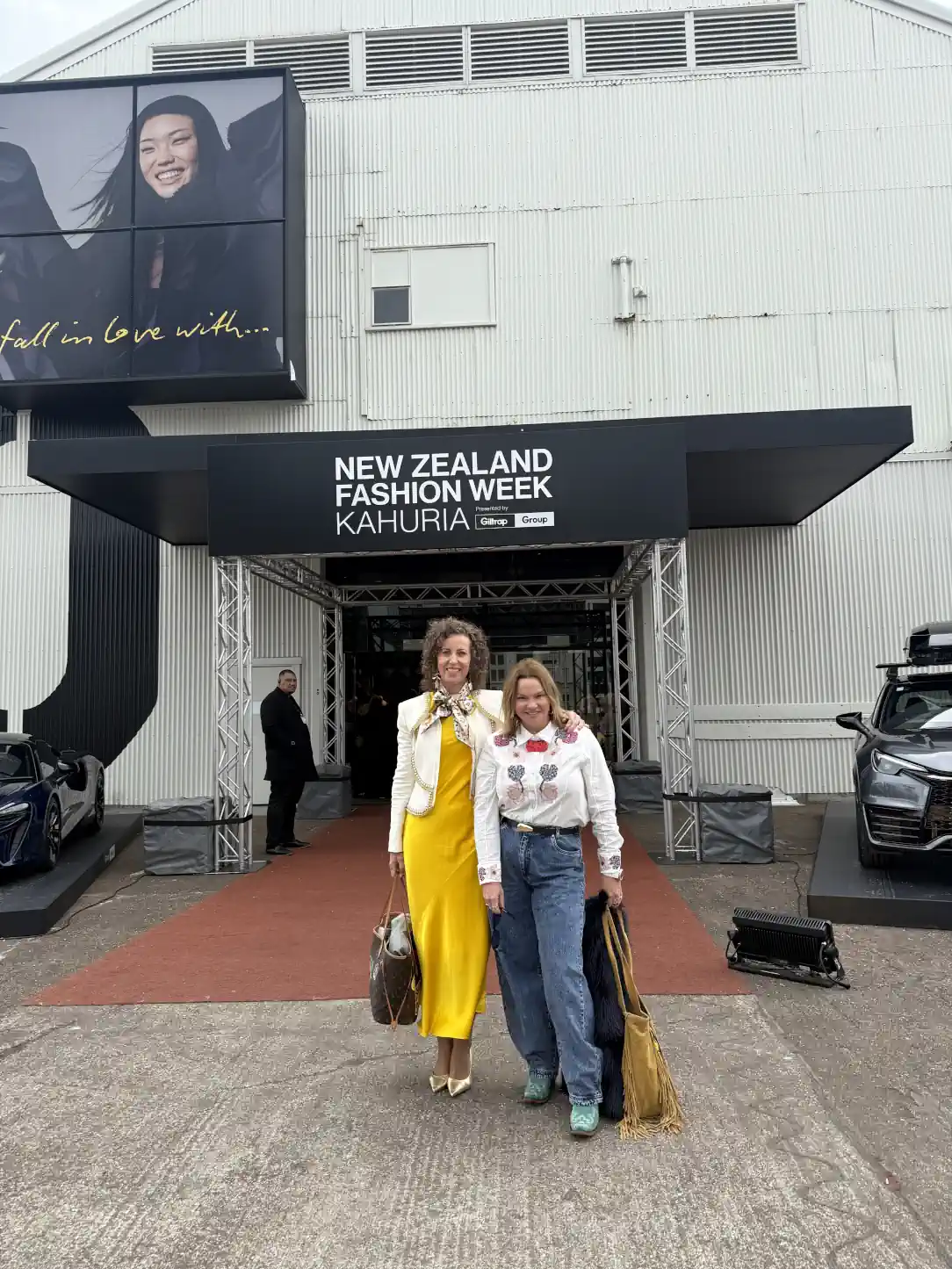 Stephanie Rumble and Rachale Davies pose together outside New Zealand Fashion Week, both smiling and dressed in chic outfits.