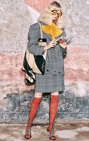 Woman in a quirky checked outfit with bold accessories, bright knee-high socks and oversized glasses, showcasing an eclectic, creative fashion style.