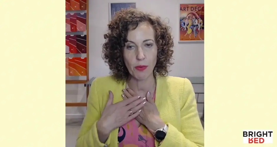 Stephanie Rumble wearing a yellow blazer places her hands on her chest while demonstrating a calming self-soothing exercise.