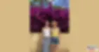 Lizzy and Stephanie stand smiling in front of a bright purple bougainvillea wall. One wears a white tank and floral skirt, the other a yellow top, shorts, and a straw hat.
