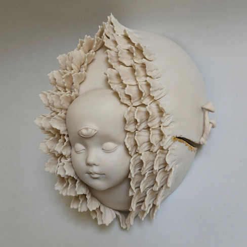 A ceramic sculpture of a baby's face with eyes closed, emerging from petals.