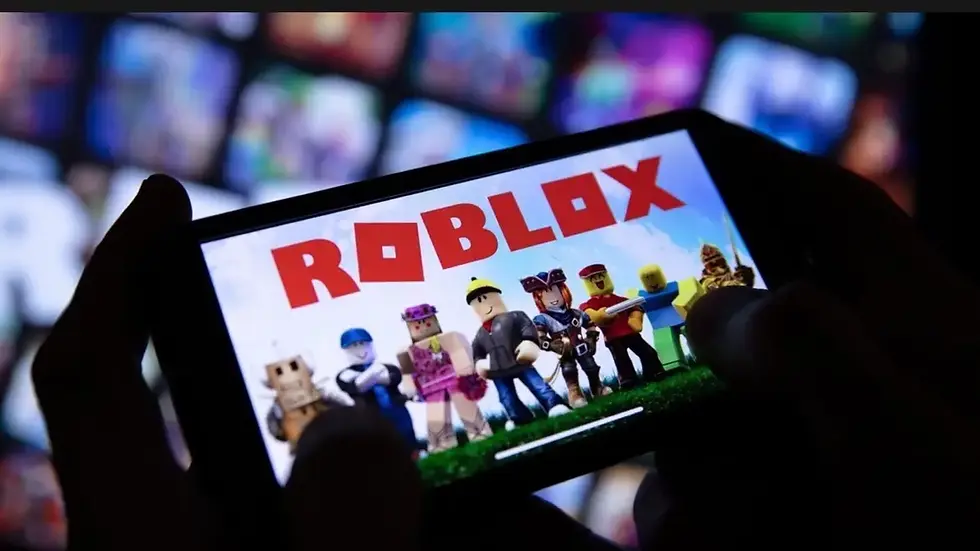 Person holds smartphone displaying Roblox characters on screen. Background shows blurred colorful shapes. Text: "ROBLOX" in bold red.