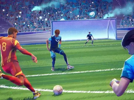 Soccer player in REMATCH video game in red kicks ball towards goal, competing against players in blue. Stadium packed with cheering fans, creating an intense atmosphere.