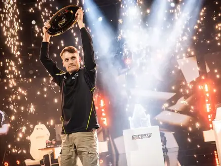Joona Serral Sotala triumphantly lifts SC2 trophy amidst fireworks at Esports World Cup stage. Bright lights and cheering create a celebratory atmosphere.
