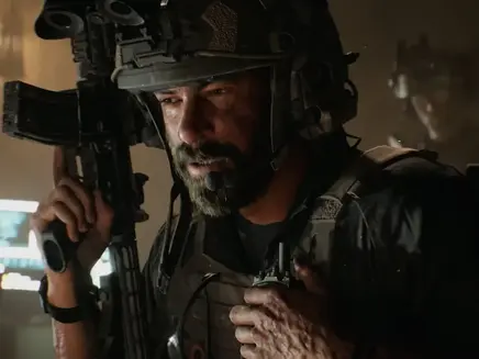 Soldier in tactical gear holds a rifle, dimly lit room with glowing screens. Serious expression, intense mood. Another figure in background. Its Battlefield 6 story trailer.