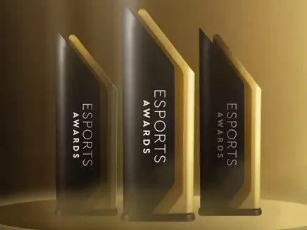 Three sleek black and gold Esports Awards trophies stand on a podium. The background is a warm gradient of gold tones, creating a prestigious mood.