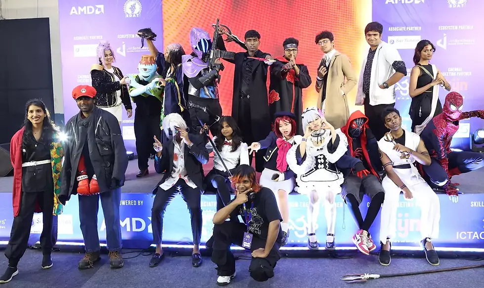Group of people in colorful costumes posing on stage. Vibrant lights, enthusiastic mood. Background features AMD logos and text. its from Chennai Thiruvizha.