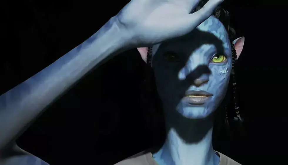 Avatar: Frontiers of Pandora character Blue-skinned humanoid with yellow eyes holds hand on forehead, casting shadows. Dark background, ethereal and mysterious mood.