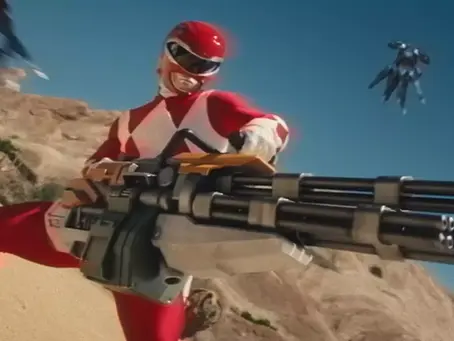 Red superhero in a desert landscape, holding a large futuristic weapon. Blue sky and scattered rocks in the background. Dynamic action pose. its Power Rangers in Fortnite c6s4.
