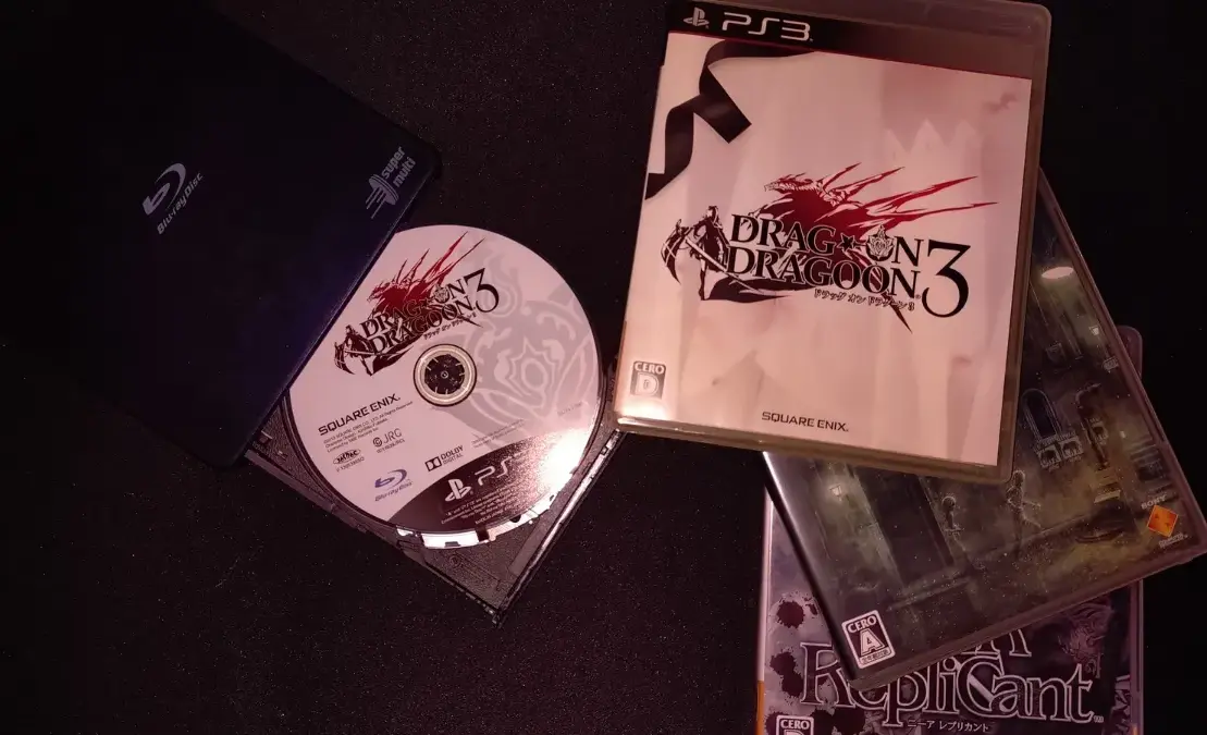 PS3 game cases and a disc for Dragon Dragon 3 and Drakengard/Replicant on a dark tabletop, with Japanese cover art.