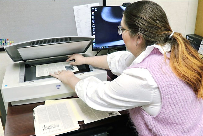Image of woman in pink sweater vest putting an archival document on a scanner