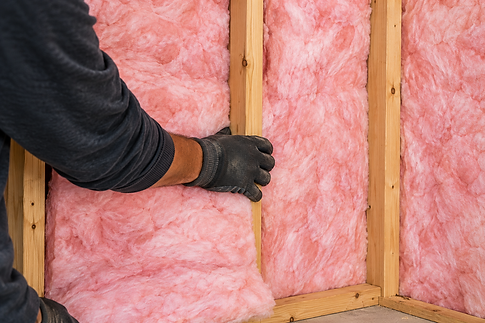 Worker installing pink fiberglass insulation between wood wall studs.