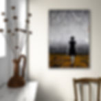 Landscape art of woman walking barefoot in yellow grass towards grey city, hanging on white wall above brown chair