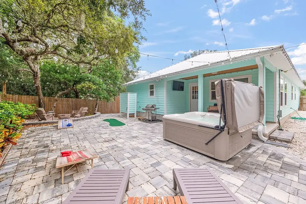 Turquoise cottage patio with hot tub, lounge chairs, cornhole, and grill surrounded by shade trees, ideal for shoulder