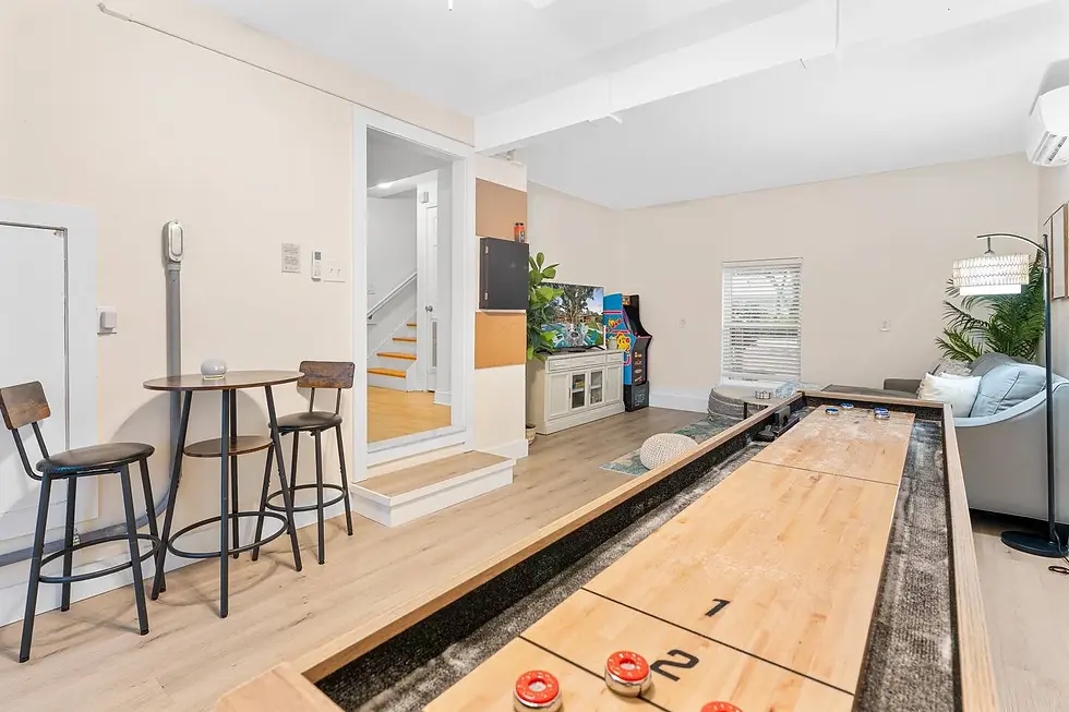 Professional listing photography of luxury villa game room with shuffleboard table, arcade machine, and bar seating in St.