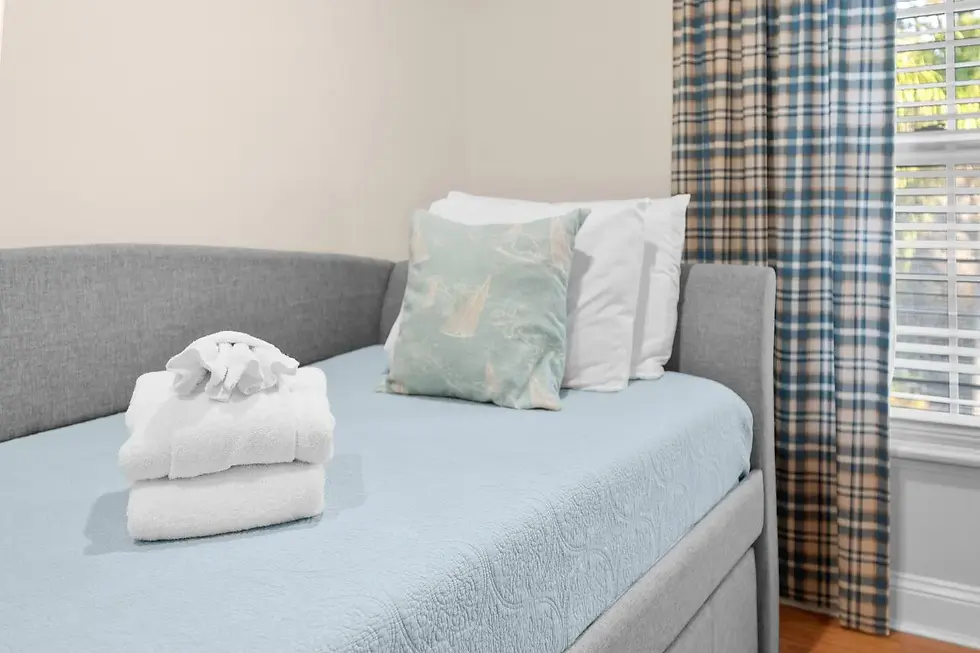 Bedroom with light blue bed, white towels, green coastal pillow, and blue plaid curtains in a vacation rental decorated with