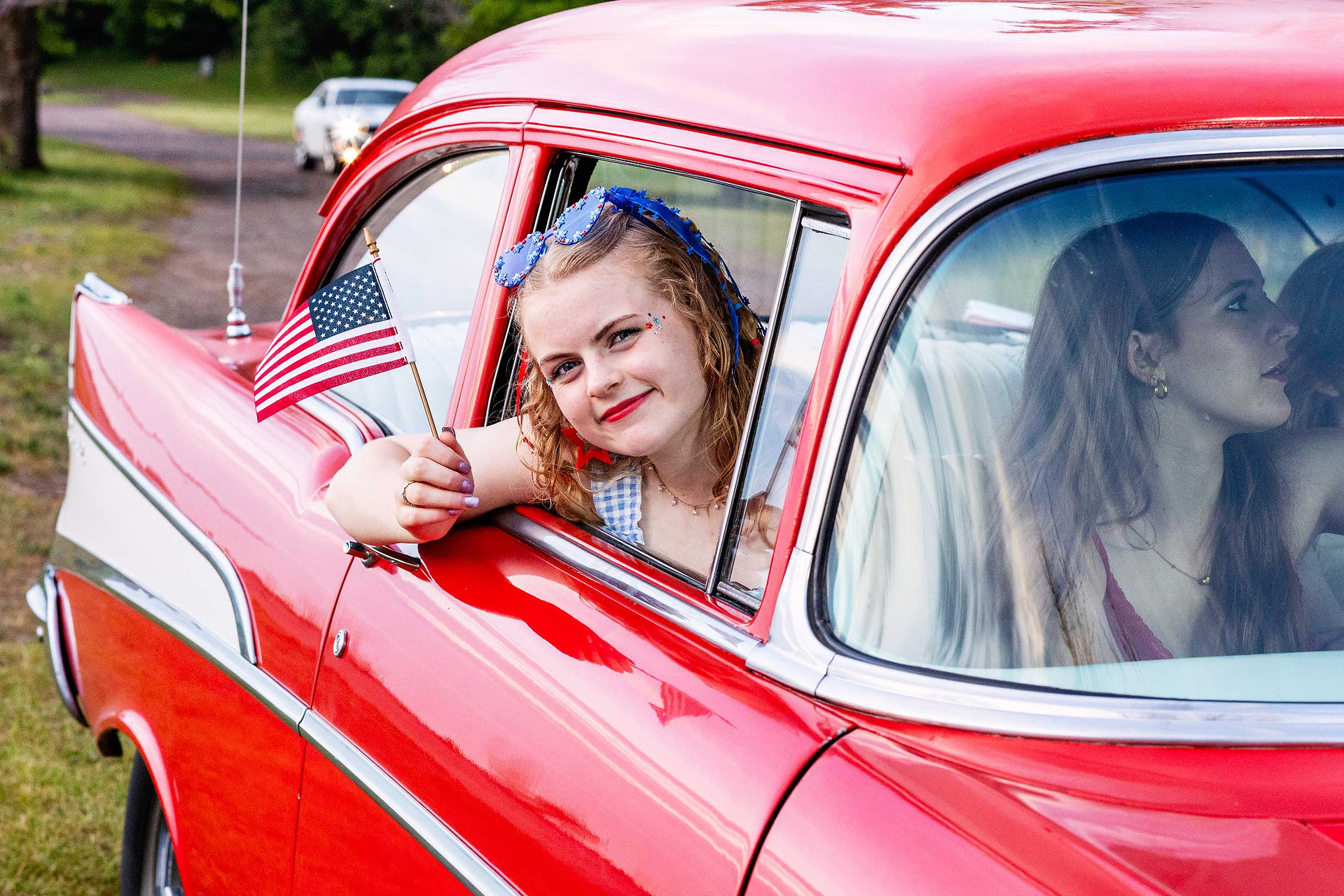 girl holding an American flag in a red 1957 chevy