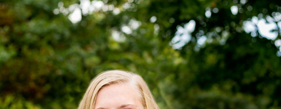 A high school senior girl leaning on a fence smiling at the camera
