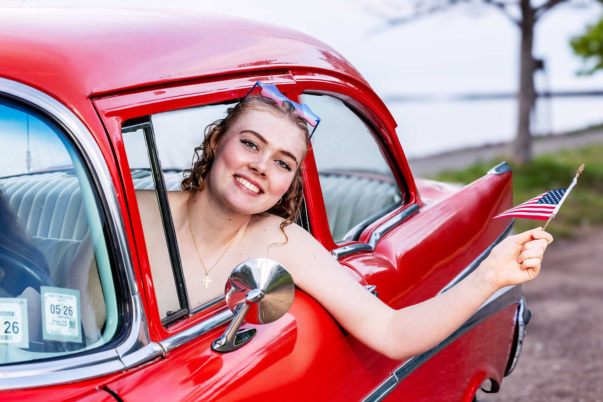 girl holding an American flag in a red 1957 chevy