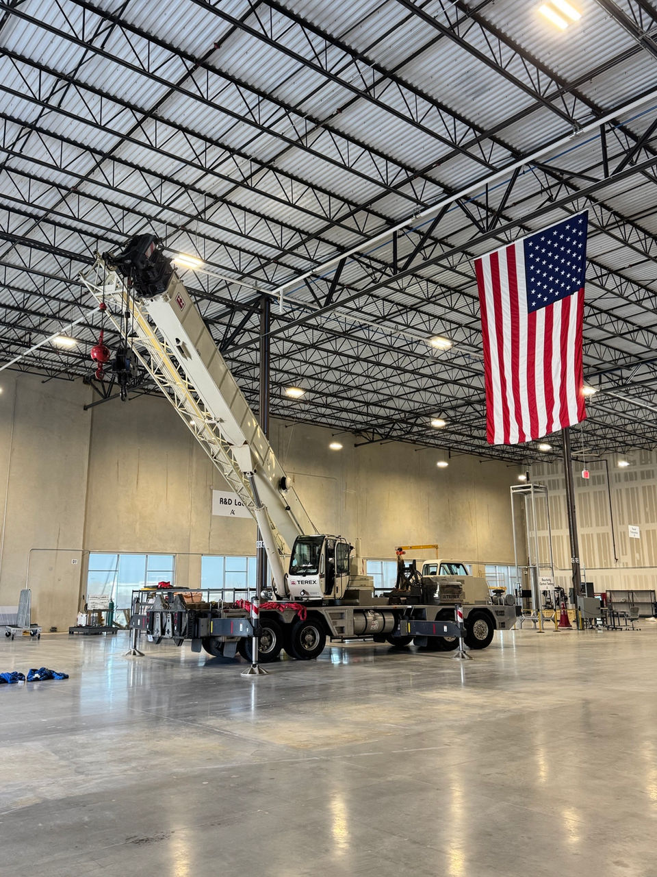 Mobile crane truck with extended boom in large warehouse, American flag.