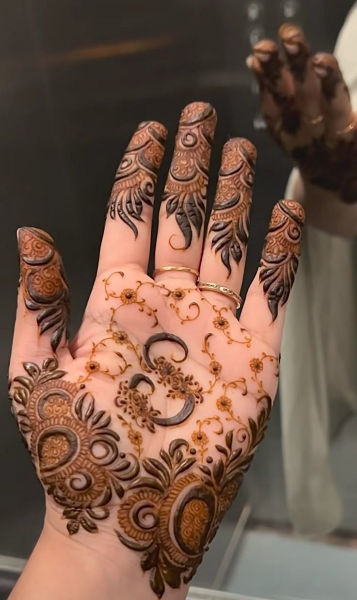 Front-hand mehndi design with bold floral swirls, leafy fingertips, and fine vine detailing