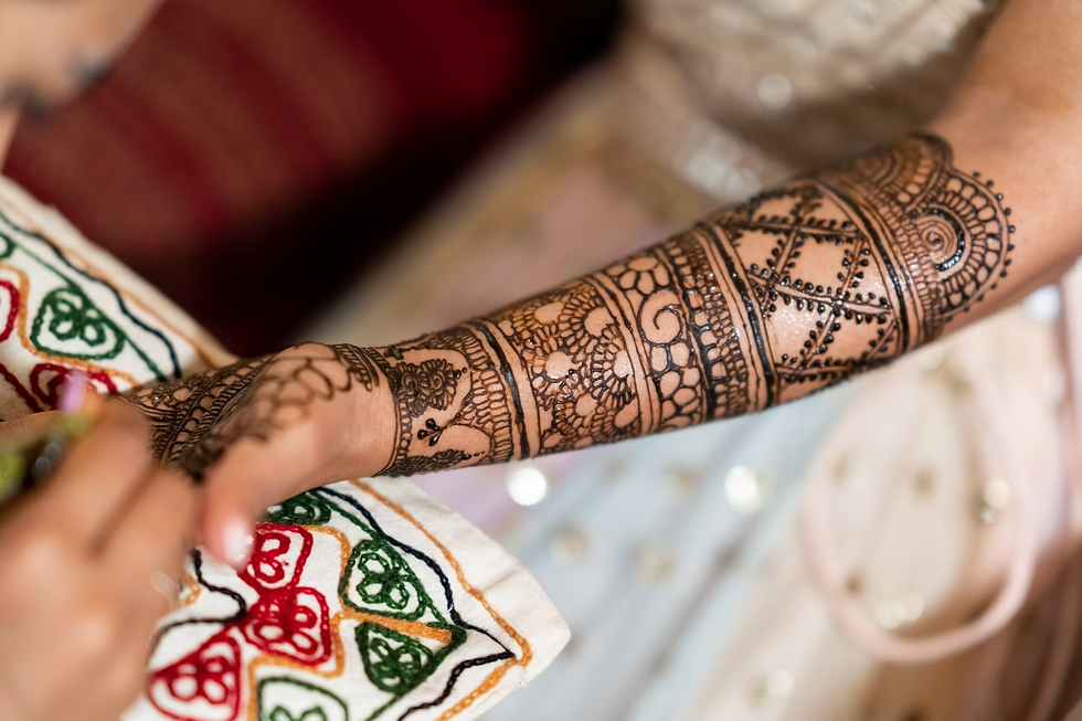 hand being adorned with a detailed front hand mehandi pattern extending from the fingers to the elbow, featuring floral and netted motifs.