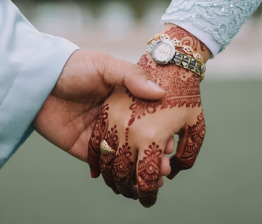 Close-up of a bride’s hand with red mehndi featuring floral details and fingertip fill