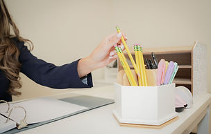 Woman's hand reaches for a yellow pencil, desk with office supplies background.