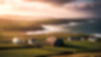 Sunlit coastal farmland with scattered cottages, green fields, cliffs and choppy sea under dramatic storm clouds at sunset