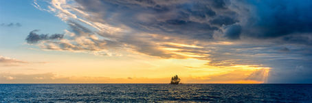 A small ship on the horizon with clear skies on the left and stormy skies on the right.