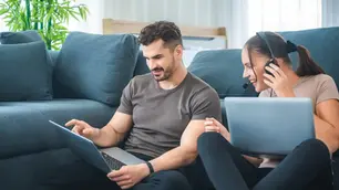 Couple sitting in the sofa watching laptops