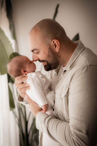 Vader met pasgeboren newborn baby bij het raam aan huis tijdens een newborn fotoshoot met daglicht