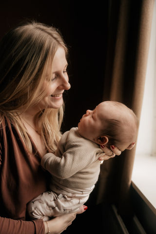 Moeder met pasgeboren newborn baby bij het raam aan huis tijdens een newborn fotoshoot met daglicht